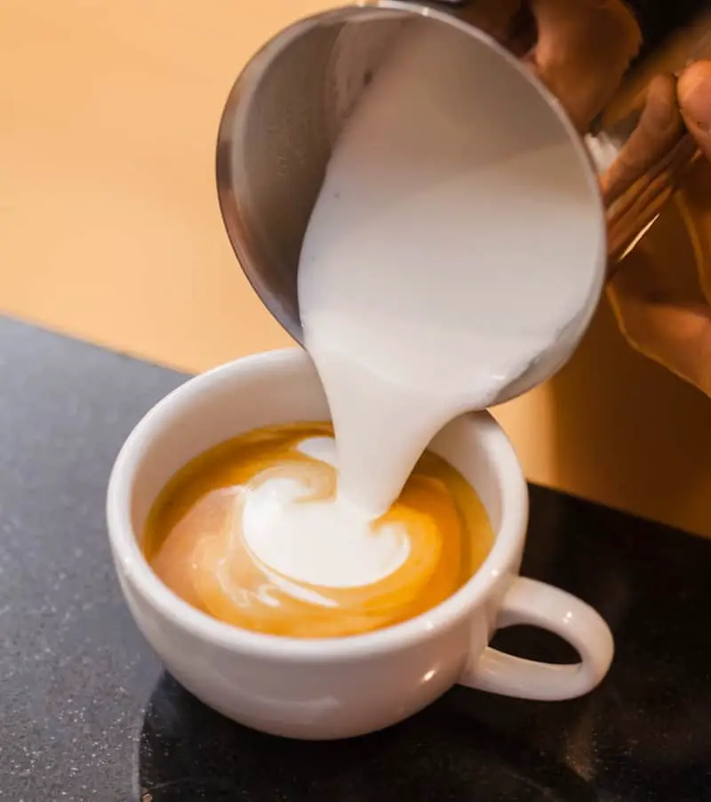 Pouring steamed milk on top of espresso to prepare a flat white coffee