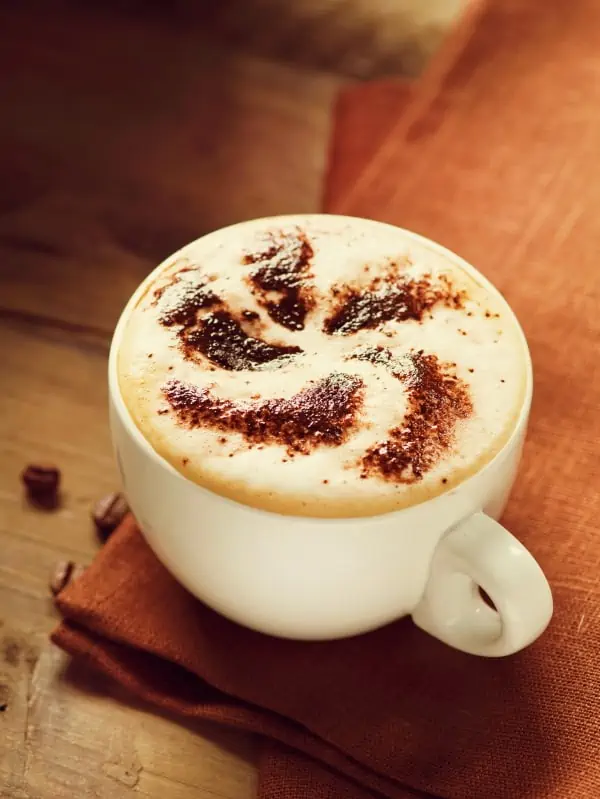 Cappuccino cup with cocoa on top to symbolize whether a cappuccino tastes sweet and whether it contains sugar.
